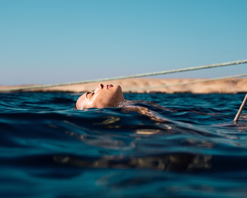 person-floating-water-sandy-shore-clear-sky.jpg